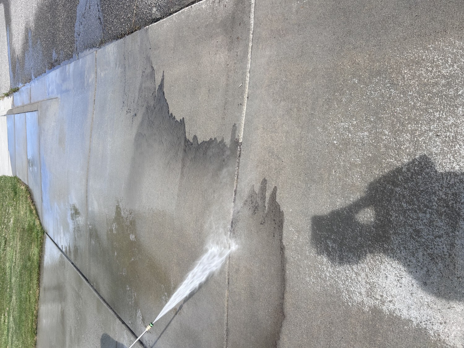 Pressure washer cutting a clean line across a concrete driveway