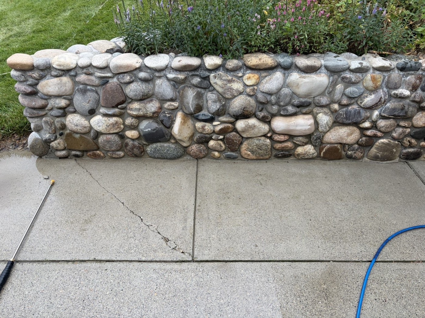 Clean sidewalk beside a river-rock wall after washing